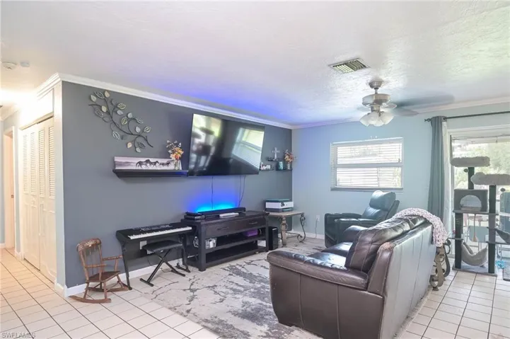 Living room featuring crown molding, ceiling fan, and light tile patterned floors