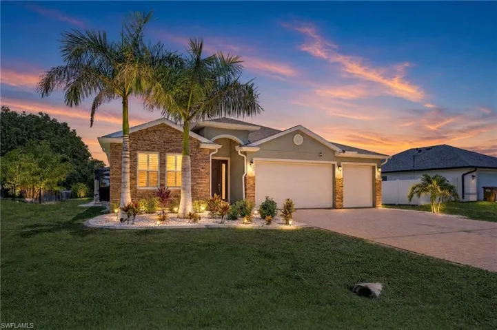 Twilight exterior showcasing exceptional curb appeal in this newer construction Cape Coral home, featuring upgraded exterior lighting, tropical landscaping, and a welcoming front elevation designed to stand out in the Northwest Cape.