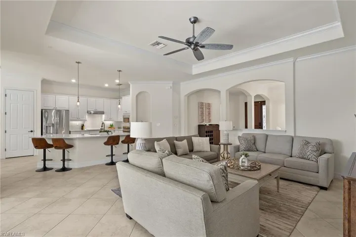 Living room featuring a tray ceiling, ceiling fan, light tile patterned floors, and crown molding