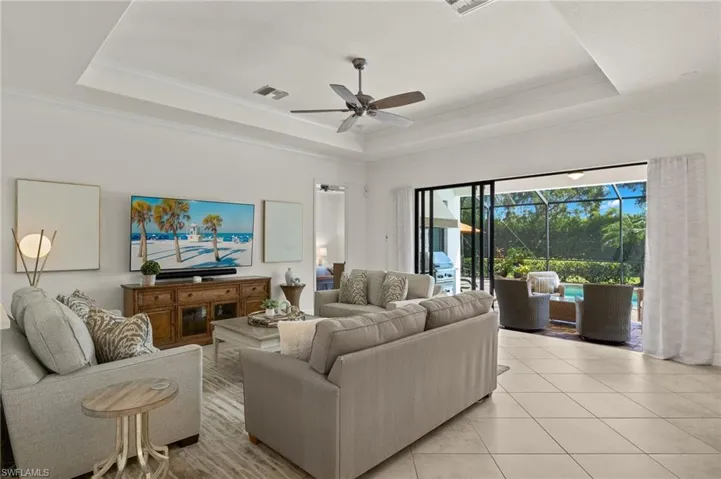 Living room with ceiling fan, a tray ceiling, crown molding, and light tile patterned floors