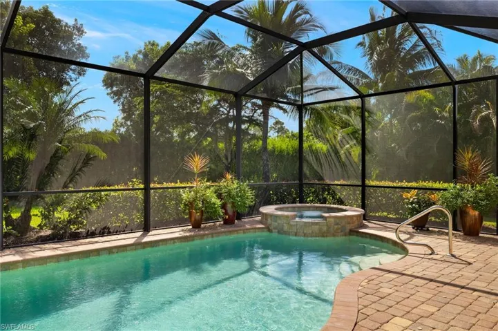 View of swimming pool featuring glass enclosure, an in ground hot tub, and a patio area
