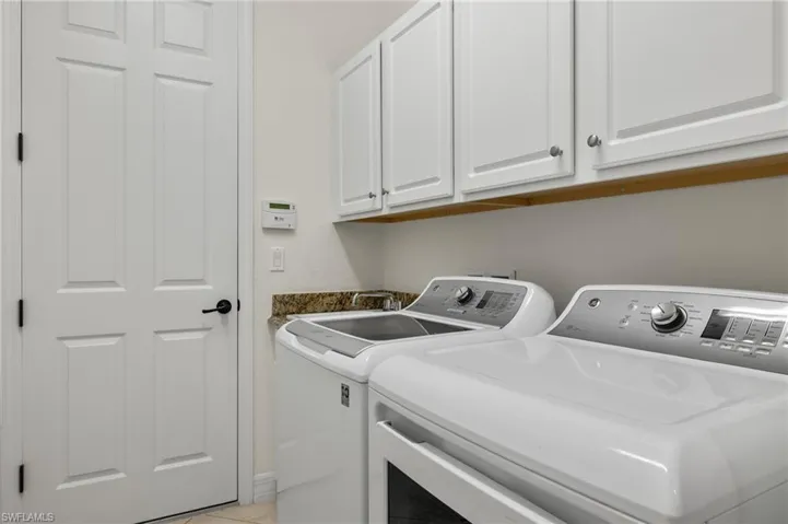 Laundry area with light tile patterned flooring, washing machine and clothes dryer, and cabinets