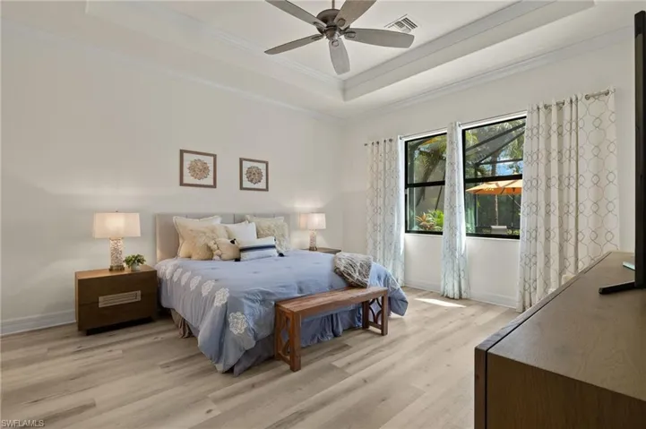 Bedroom with ceiling fan, light wood-type flooring, crown molding, and a raised ceiling
