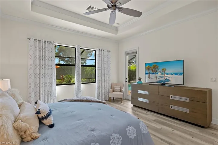 Bedroom with ornamental molding, light hardwood / wood-style floors, a tray ceiling, and ceiling fan