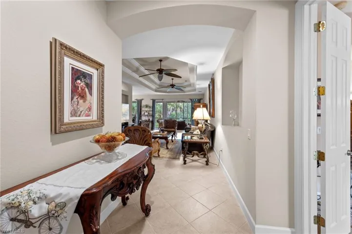Corridor featuring a tray ceiling, light tile patterned floors, and arched walkways