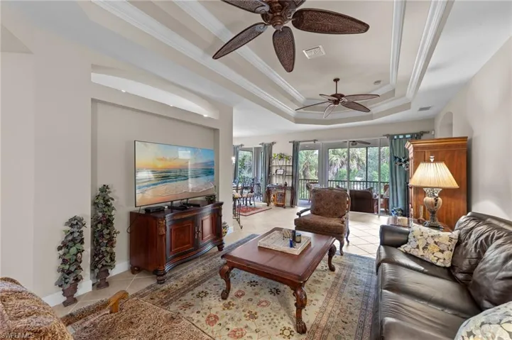 Living area with a raised ceiling, ornamental molding, light tile patterned floors, and ceiling fan
