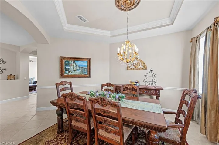 Dining space featuring arched walkways, a tray ceiling, light tile patterned floors, ornamental molding, and a chandelier
