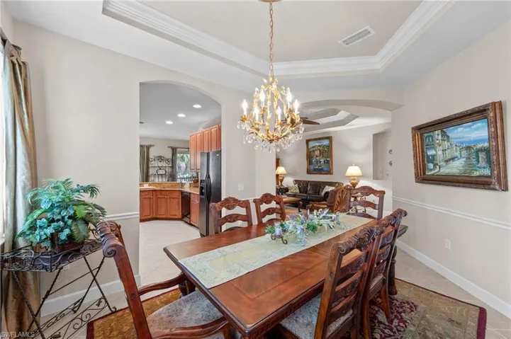 Dining area with arched walkways, a tray ceiling, a chandelier, and crown molding