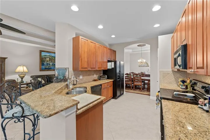 Kitchen with black appliances, light stone counters, a peninsula, hanging light fixtures, and recessed lighting