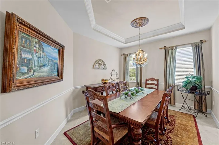 Dining space with a raised ceiling, a chandelier, ornamental molding, and light tile patterned flooring