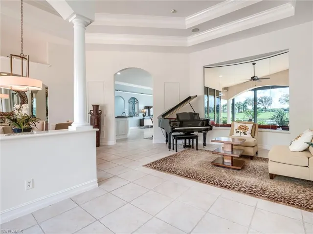 Tiled living room featuring ceiling fan, a tray ceiling, crown molding, and decorative columns