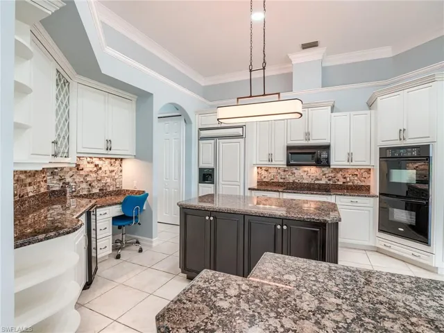 Kitchen featuring dark stone countertops, a center island, built in desk, and black appliances