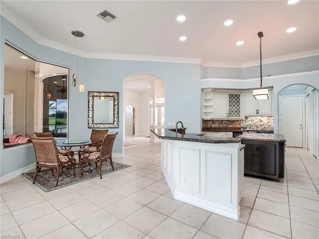 Kitchen with light tile patterned flooring, ornamental molding, a kitchen island, decorative light fixtures, and decorative backsplash