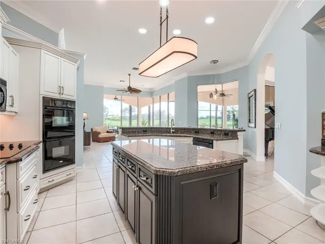 Kitchen featuring light tile patterned floors, black appliances, crown molding, a center island, and dark stone counters