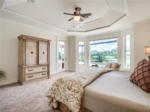 Bedroom with a tray ceiling, ceiling fan, multiple windows, and access to outside
