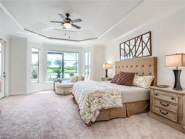 Carpeted bedroom featuring ceiling fan, a raised ceiling, and crown molding
