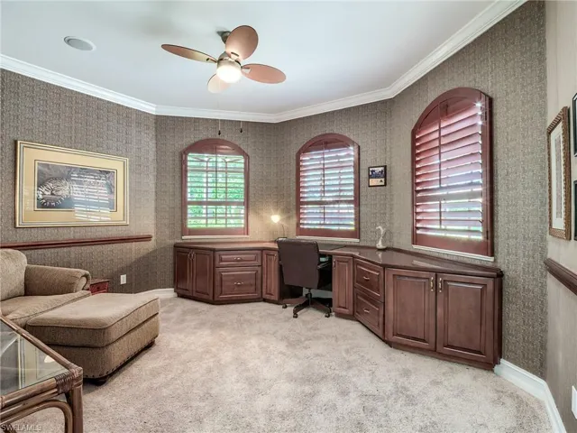 Carpeted office space with built in desk, ornamental molding, and ceiling fan