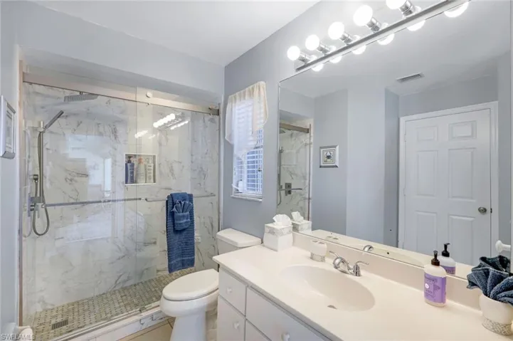 Bathroom with visible vents, toilet, vanity, and a marble finish shower