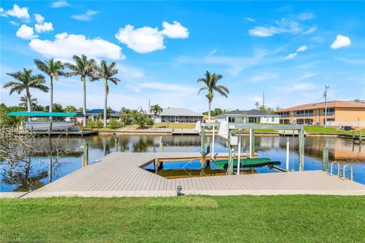 View of dock with a lawn, a water view, boat lift, and a residential view