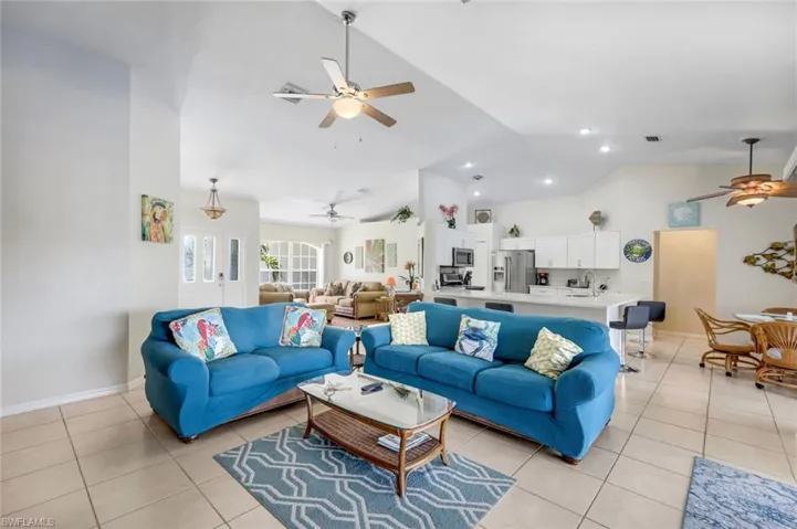 Living area with light tile patterned floors, visible vents, baseboards, lofted ceiling, and ceiling fan