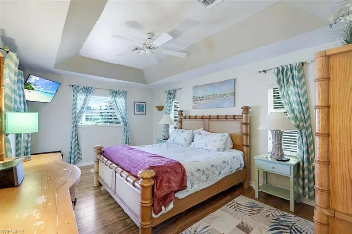 Bedroom with ceiling fan, wood finished floors, visible vents, baseboards, and a tray ceiling