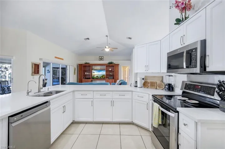 Kitchen with stainless steel appliances, light countertops, light tile patterned flooring, vaulted ceiling, and a sink