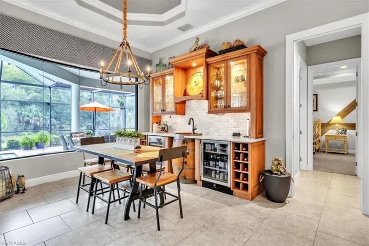 Custom built-in bar featuring wood cabinetry, glass-front display shelving, stone-tiled backsplash, integrated wine refrigeration, and a barrel-base sink console