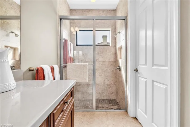 Bathroom featuring stone-tile wall finishes, shower with a glass enclosure, built-in shower niche, light-toned countertop, and dark-finish wood cabinetry