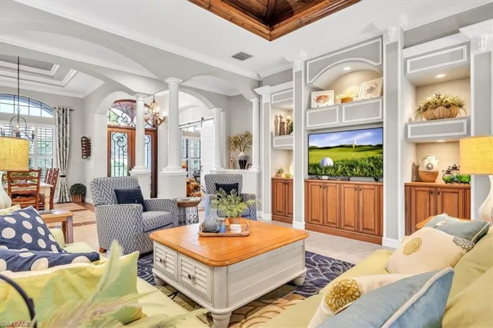 Custom built-in cabinetry with recessed lighting, recessed ceiling featuring wood-finish detailing, architectural columns, and arched wall openings
