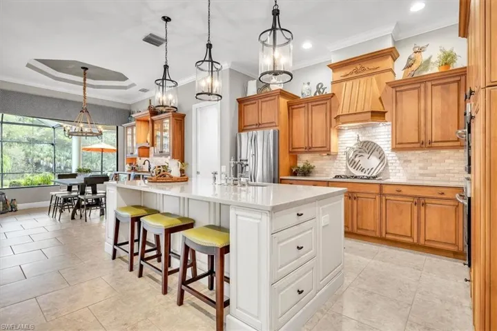 Kitchen featuring a center island with a white cabinetry base, stone-surface countertops, wood cabinetry, a tiled backsplash, and multi-light hanging fixtures