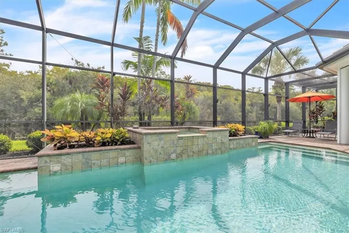 Screened pool enclosure featuring a built-in spa with stone-finish tiling and elevated planter boxes