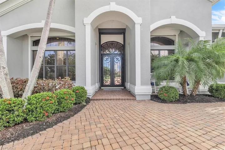 Stucco exterior featuring dual arched entryways, a brick-paved walkway, and an ornate wrought-iron double front door with an arched transom window