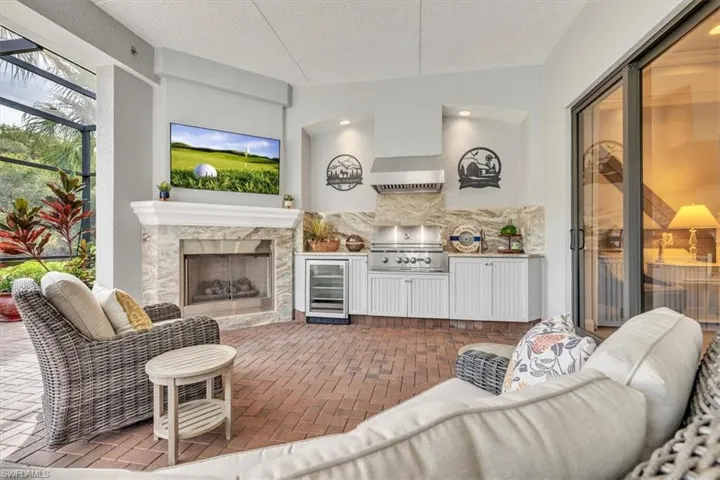 Covered lanai featuring a stone-surround fireplace, built-in outdoor kitchen with a stainless steel range hood, integrated beverage refrigerator, and brick paver flooring
