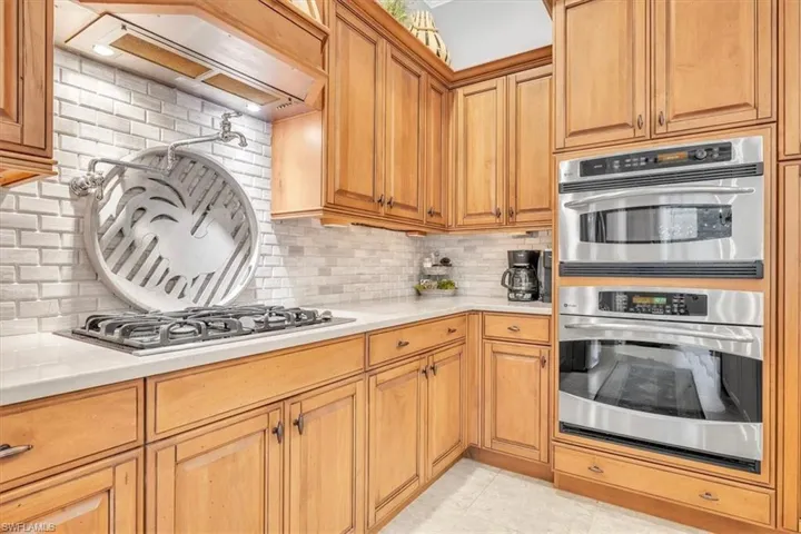 Kitchen featuring wood cabinetry, stainless steel built-in double wall ovens, a gas cooktop, brick-style tile backsplash, and light-toned solid surface countertops