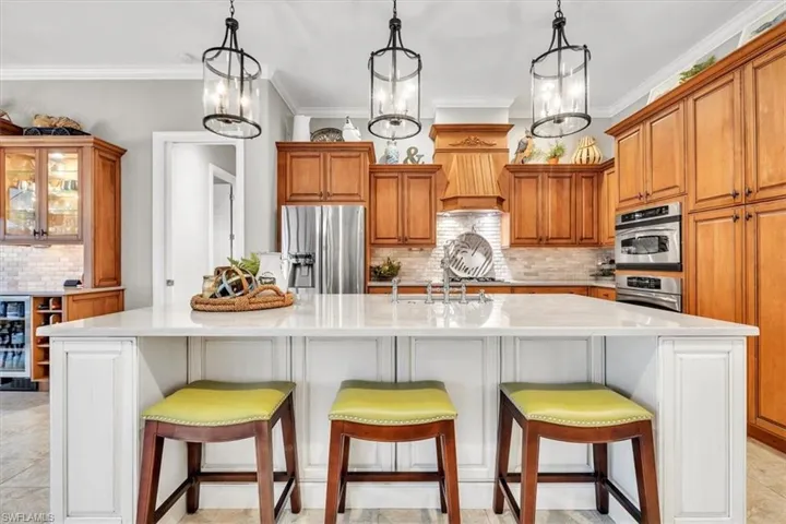 Kitchen featuring a large central island with a white countertop, stained wood cabinetry, stainless steel double wall ovens, glass-front display cabinets, and three metal lantern-style pendant lights
