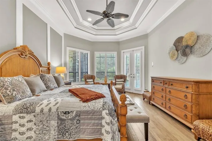 Tray ceiling with crown molding, wood-finish flooring, recessed lighting, ceiling fan, and double glass-panel doors