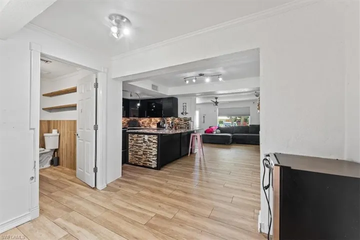 Kitchen featuring crown molding, open floor plan, light wood-type flooring, ceiling fan, and dark cabinets