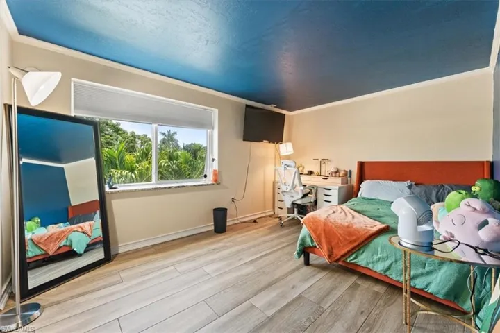 Bedroom featuring wood finished floors, ornamental molding, and an office area
