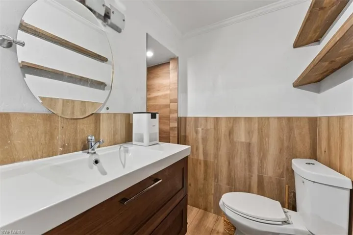 Half bathroom with vanity, crown molding, and wainscoting