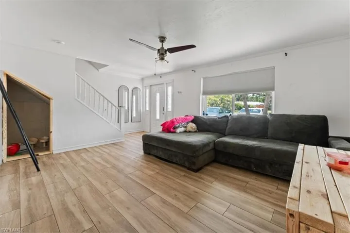 Living room with light wood-style flooring, stairs, ceiling fan, and crown molding