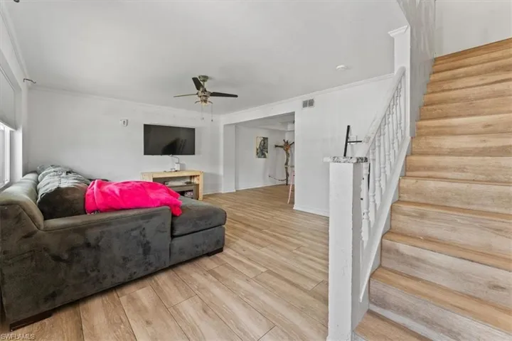 Living area featuring stairway, ceiling fan, crown molding, and wood finished floors