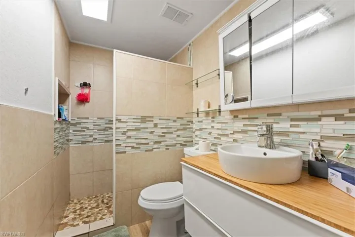 Bathroom with a walk in shower, vanity, tasteful backsplash, and tile walls