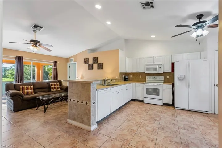 Kitchen with kitchen peninsula, sink, vaulted ceiling, white cabinetry, and white appliances