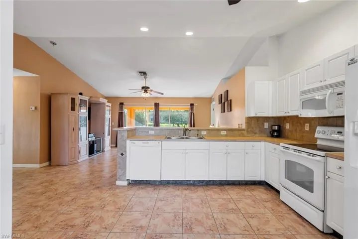 Kitchen with white appliances, lofted ceiling, kitchen peninsula, and sink