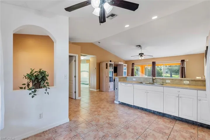 Kitchen with lofted ceiling, kitchen peninsula, white cabinetry, dishwasher, and sink