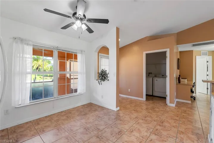 Empty room featuring vaulted ceiling, light tile patterned flooring, separate washer and dryer, and ceiling fan