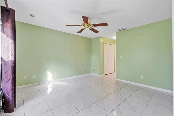 Empty master bedroom featuring light tile patterned floors and ceiling fan