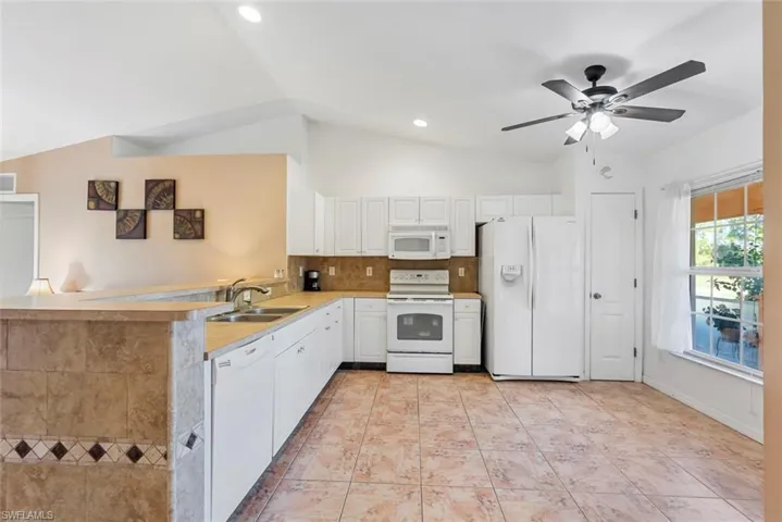 Kitchen featuring white appliances, sink, white cabinetry, lofted ceiling, and light tile patterned floors