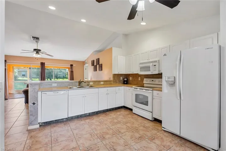 Kitchen featuring kitchen peninsula, sink, light tile patterned floors, white cabinets, and white appliances