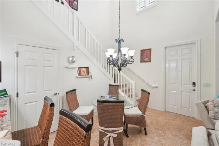 Dining area featuring a chandelier, light tile patterned flooring, a towering ceiling, baseboards, and stairs